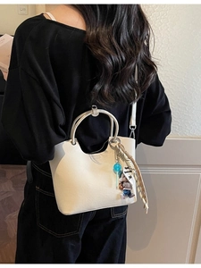 Chic beige bucket bag with metal ring handle and cute doll charm worn as crossbody bag