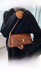 Close-up of brown vintage leather baguette bag with a golden metal clasp on shoulder