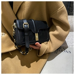 Détail du sac bandoulière noir en cuir avec fermoir doré porté sur un manteau beige