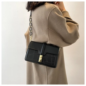 Détail du sac bandoulière noir avec texture croco et fermoir doré sur un manteau beige