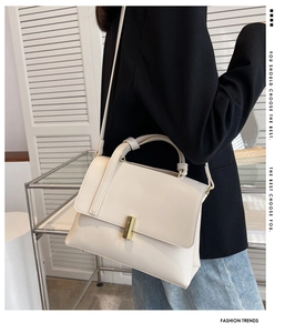 Gros plan d'un sac bandoulière crème avec détails dorés porté par un mannequin en blazer