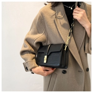 Gros plan du sac bandoulière noir à motif crocodile avec fermoir rotatif doré