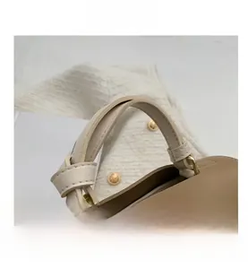 Détail d'un sac à main beige en cuir avec boucle dorée sur un tissu texturé