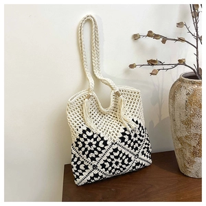 Detail of woven tote bag featuring black and white geometric patterns and tassel accents