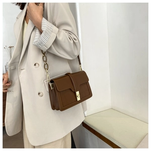 Détail du sac bandoulière marron motif pierre avec boucle dorée sur blazer blanc