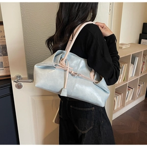 Détail du sac cabas bleu clair en similicuir avec anses beiges porté à l'épaule du mannequin