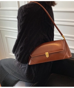Close-up of a vintage brown leather baguette bag with a gold clasp on a model