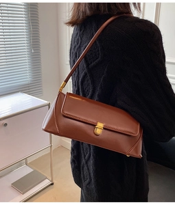 Side view of a vintage brown leather baguette bag with a gold buckle on black sweater