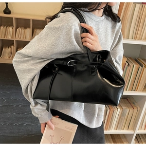 Détail du sac cabas en cuir noir avec boucle sur un mannequin devant une bibliothèque