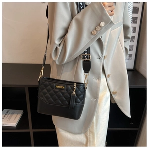 Close-up of black quilted leather crossbody bag with gold hardware and geometric wide strap