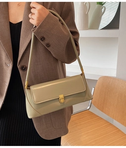 Close-up of sage green baguette bag with golden metal clasp and smooth leather texture