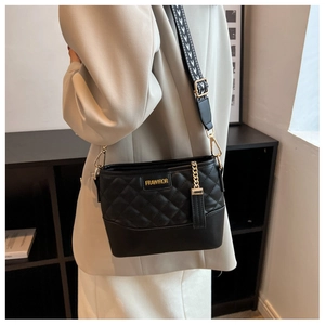 Detail of black quilted bucket bag with geometric strap and gold chain hardware