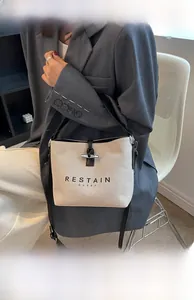 Detail of canvas bucket bag featuring black leather trim and RESTAIN EVERY printed text