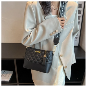 Detail of black quilted shoulder bag with wide pattern strap and gold hardware accents