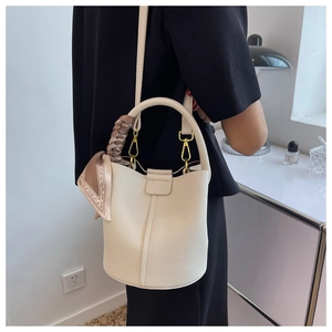 Détail d'un sac seau en cuir crème avec foulard en soie porté par un mannequin chic