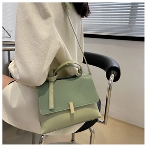 Détail d'un sac à bandoulière vert clair porté par un mannequin dans un bureau moderne
