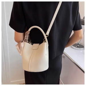 Détail du sac seau blanc crème texturé avec un foulard en soie enroulé sur la poignée