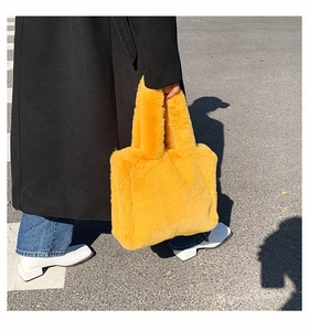 Street style shot of a bright yellow faux fur tote bag with a black wool coat