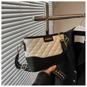 Close-up of quilted white leather bag with gold logo and patterned wide strap