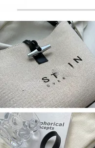 Detail of cream canvas tote bag with black leather strap and metallic T-bar clasp
