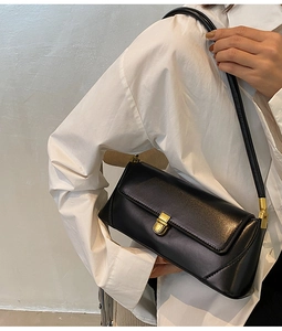 Detail of black leather underarm bag with gold clasp shown on a white shirt