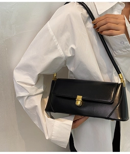 Detail of black leather underarm bag with gold twist lock on a white shirt