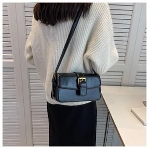 Detail of a black patent leather crossbody bag with gold hardware on a model