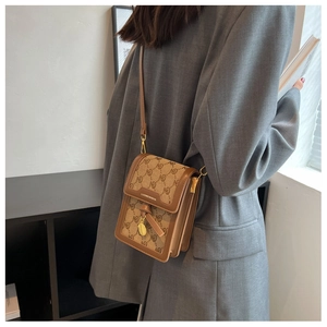 Detail of vintage patterned crossbody bag with leather trim worn on a grey blazer