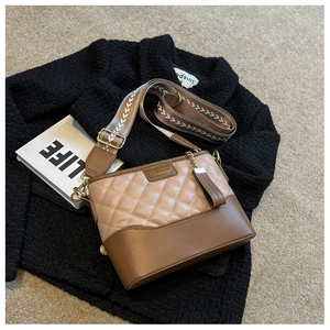 Detail of quilted leather bucket bag with wide patterned strap and metal brand logo