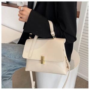 Sac à main chic en cuir crème avec fermoir doré porté avec une veste blazer noire
