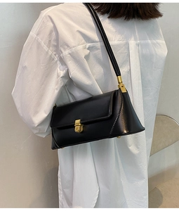 Detail of a chic black baguette bag with gold metal buckle on a white shirt