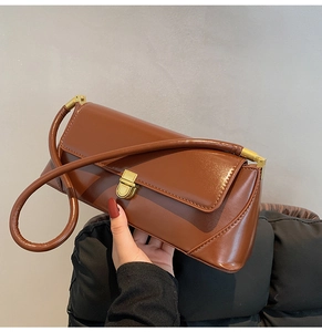 Detail of brown leather baguette bag featuring a gold rectangular clasp and fine texture