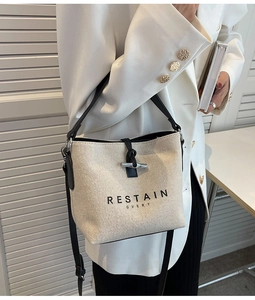 Close-up of canvas bucket bag with leather accents and buckle on model's white blazer