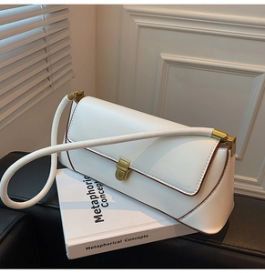 Detail of white baguette bag with brown piping and golden clasp on a book