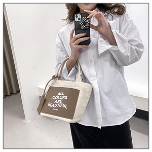 Detail of canvas tote bag with brown leather pocket and white inspirational slogan