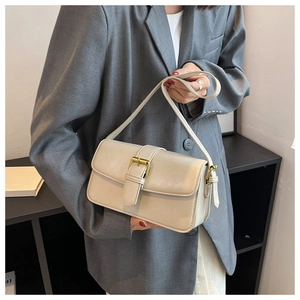 Detail of minimalist beige rectangle shoulder bag with gold metal buckle on a grey blazer
