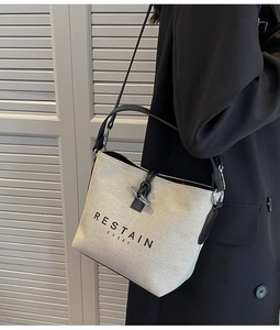 Detailed macro of cream canvas bucket bag featuring black lettering and metal T-bar closure