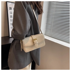 Close-up of a cream crossbody bag with gold hardware worn over a grey blazer