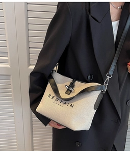 Detail of canvas crossbody bag with leather trim and metal toggle closure on shoulder