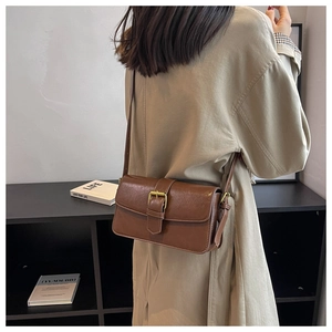 Lifestyle shot of a vintage brown crossbody bag with gold buckle on a shoulder model