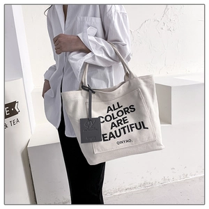 Off-white canvas tote bag with black letter slogan and front pocket worn by a model