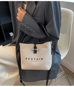 Detail of canvas bucket bag with black leather trim and logo lettering on front