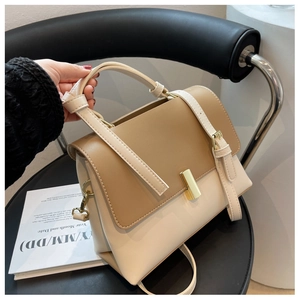 Détail d'un sac bandoulière rétro kaki et beige avec fermoir doré posé sur une chaise