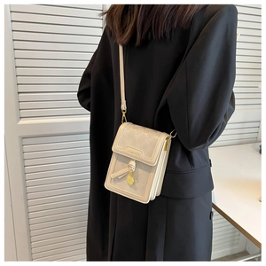 Detail of cream crossbody bag with embossed texture and gold charm shown on model