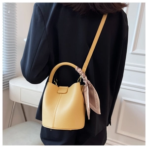 Détail du sac seau jaune en cuir grainé avec foulard en soie rose noué sur l'anse
