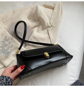 Top view of a black leather baguette bag with a gold metal clasp and protective studs