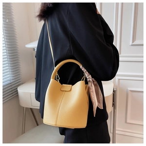Détail du sac seau en cuir jaune avec foulard en soie lilas sur un blazer noir élégant