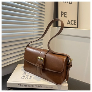 Detail of vintage brown baguette bag with golden buckle on white book prop
