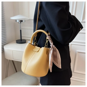 Détail d'un sac seau en cuir jaune avec foulard en soie sur la poignée et bandoulière