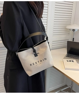 Model wearing a cream canvas bucket bag with black leather trim and horn buckle closure